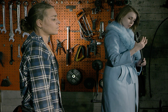 Kaksi henkilöä seisoo työkaluseinän edessä, oikeat kyljet kohti kameraa. Toinen pitää käsissään isoa jakoavainta ja katsoo sitä.