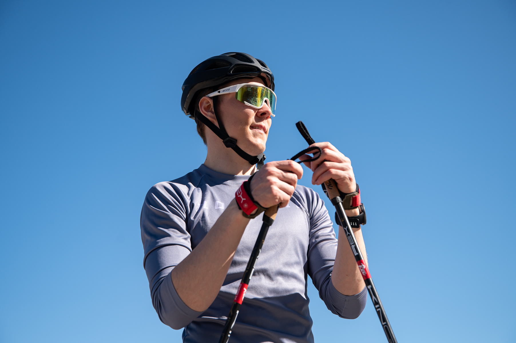 Mies aurinkolasit päässä ja kypärä päässä pitää käsissään sauvoja aurinkoista taustaa vasten.