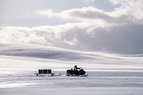 Moottorikelkka ajaa talvisessa tunturimaisemassa ja vetää perässään mobiilitekniikkarekeä.