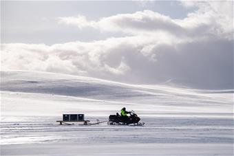 Moottorikelkka ajaa talvisessa tunturimaisemassa ja vetää perässään mobiilitekniikkarekeä.
