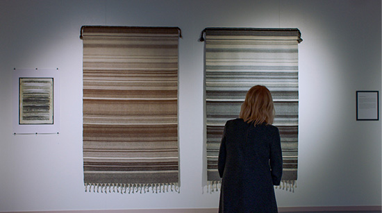 Selin oleva henkilö katsoo kahta näyttelyseinällä olevaa raanua. Kuva Maria Gullstenin elokuvasta Kaksi Kaamosta.