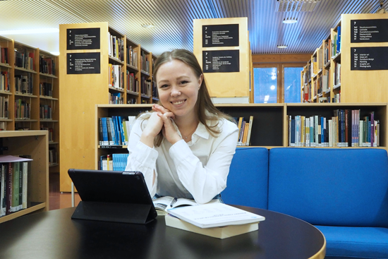 Valeriia Makeionok istuu pöydän ääressä Lapin korkeakoulukirjastossa, edessään kirjoja ja tietokone.