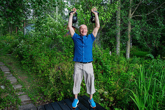 Mikko Kellokumpu seisoo pensaiden keskellä ja pitää molemmissa käsissään kahvakuulaa. 