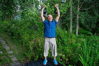 Mikko Kellokumpu seisoo pensaiden keskellä ja pitää molemmissa käsissään kahvakuulaa. 