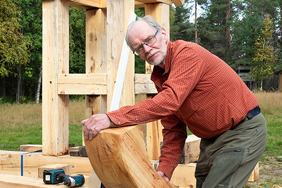Timo Jokela pitää käsissään kaarevaa hirsiveistoksen osaa. Kuva: Aki Lintumäki.