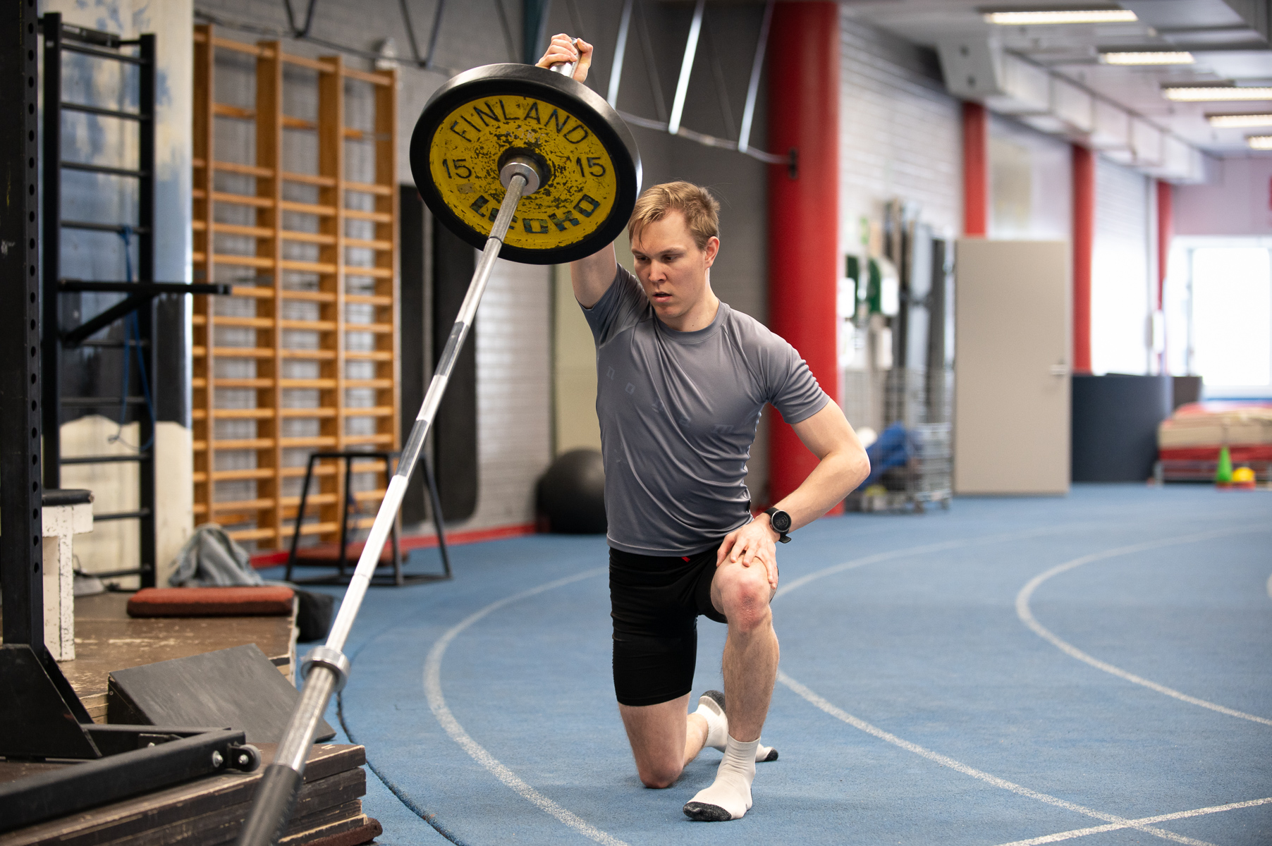 Mies nostaa yhdelle kädellä painoa, jonka toinen pää on maassa.