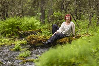 Kuvassa Eeva Rossi istuu metsässä puron varrella. 