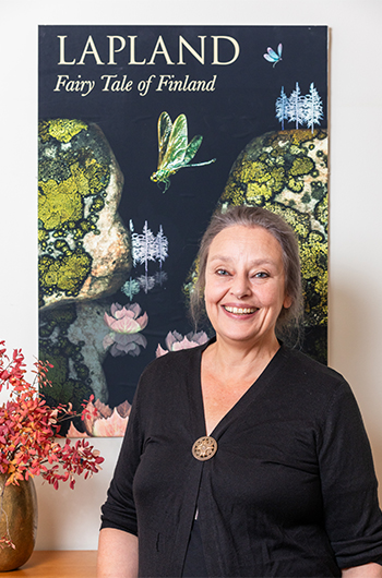Leena Raappana-Luiro, taustallaan piirrosjuliste, jossa erilaisia luontoelementtejä ja teksti Lapland - Fairy Tale on Finland.
