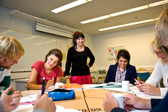 Opiskelijoita ja opettaja pyöreän pöydän äärellä.