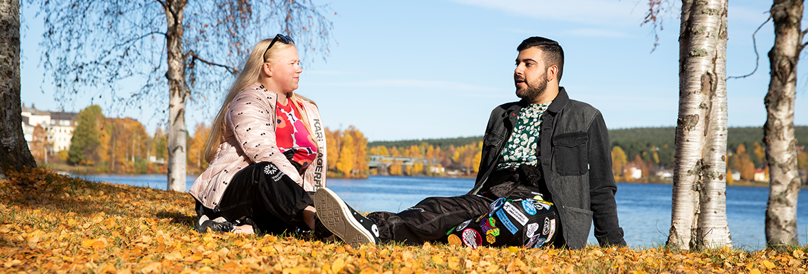 Kaksi opiskelijaa istuvat Kemijoen rannalla syksyisessä maisemassa juttelemassa