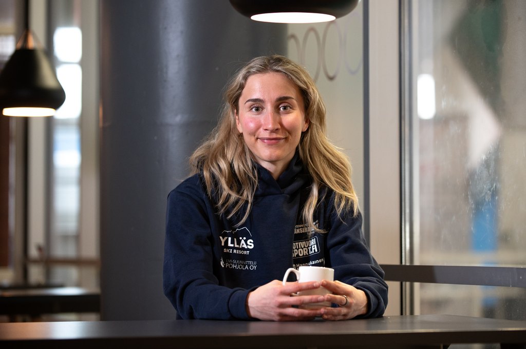 "Nainen istuu hiihtojoukkueen paita päällä kahvilassa."