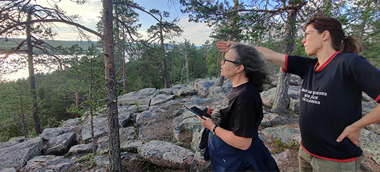 Anniina Koivurova ja Tuija Hautala-Hirvioja katsovat järvimaisemaa kivikkoisen vaaran päällä.