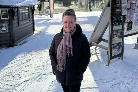 Kuvassa Mielikäinen seisoo lumisessa maisemassa, taustalla rakennuksia ja kylttejä.