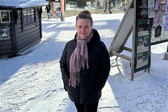 Kuvassa Mielikäinen seisoo lumisessa maisemassa, taustalla rakennuksia ja kylttejä.