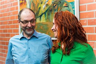 Hannele Alajoutsijärvi ja Timo Aarrevaara hymyilevät, taustalla tiiliseinä.