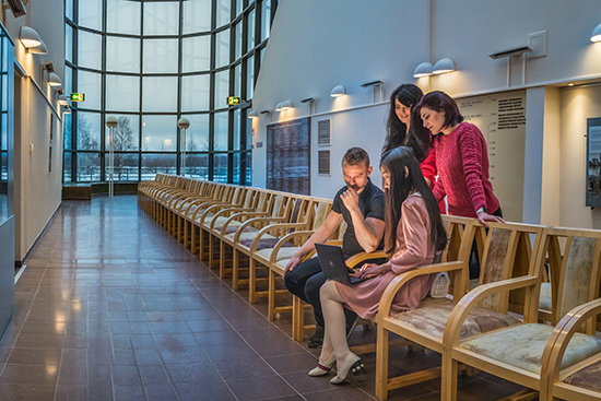 Neljä ihmistä istuvat penkkirivillä katsoen kannettavaa.