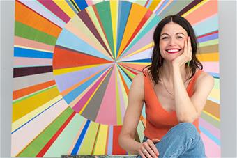 Hanna Heinonen istuu rennosti maalauksensa Cake Machine edessä. Kuva: Janne Alavahtola.