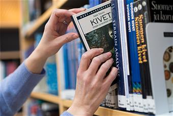 Kädet, jotka ottavat hyllystä kirjan.
