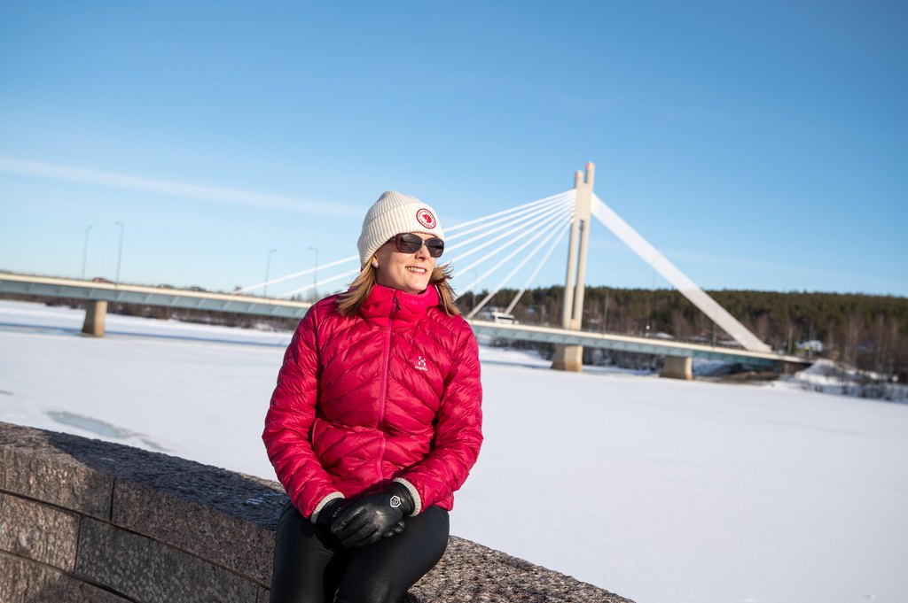 Nainen istuu kivetyksellä, taustalla talvinen Kemijoki ja Jätkänkynttilä.