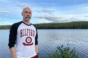 Jukka Kiviniemi seisoo joen rannassa, taustalla vaaramaisema. Kuva: Markku Ollikainen.