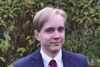 Mikko Huttunen, taustallaan vihreitä pensaita.