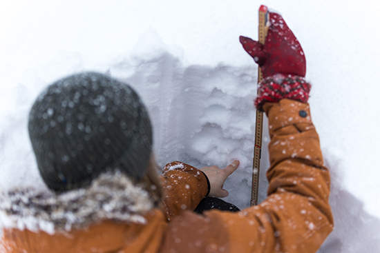 Henkilö lumikuopassa mittatikun kanssa kokeilemassa lumen kerroksia.