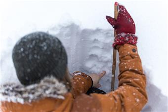 Henkilö lumikuopassa mittatikun kanssa kokeilemassa lumen kerroksia.