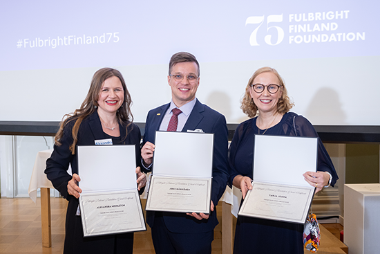 Kolme palkittua henkilöä hymyilevinä ryhmäkuvassa kunniakirjojen kera.