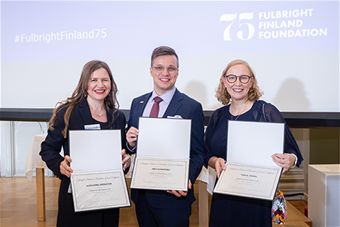 Kolme palkittua henkilöä hymyilevinä ryhmäkuvassa kunniakirjojen kera.