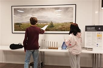 Kaksi nuorta tarkastelee Rájácummá -ympäristötaideteoksen dokumenttivalokuvaa. 