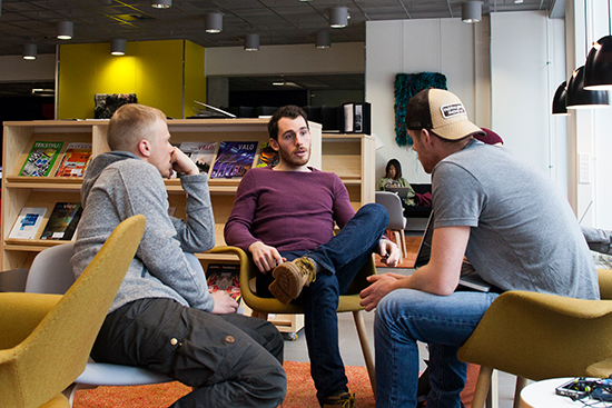 Kolme opiskelijaa istuu rennosti nojatuoleissa ja keskustelee.