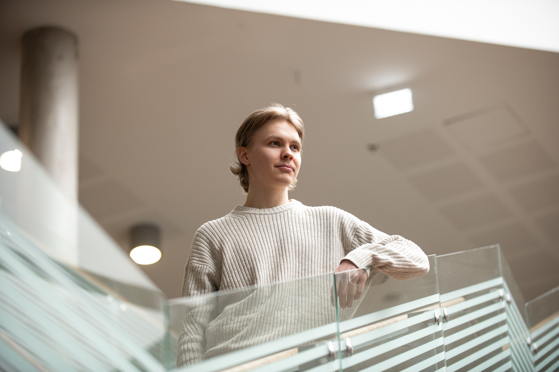 "Nuori mies villaneuleessa katsoo Lapin yliopiston Petronella-aulassa kaiteen yli."