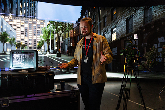 Samuli Valkama esittelee virtuaalituotantostudiota ja seisoo ison, kaarevan lediseinän edustalla, vieressään kameralaitteistoja. Kuva: Ville Rinne.