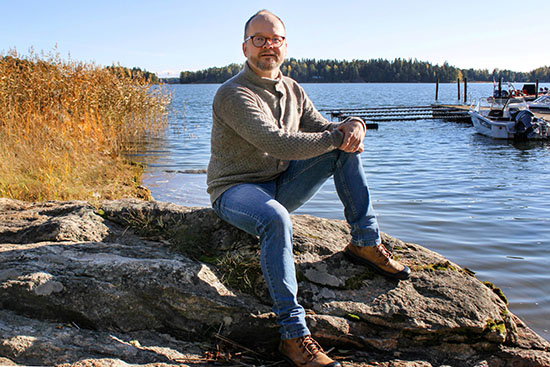 Kuvassa Vihtari istuu rantakalliolla, taustalla vene ja laituri.