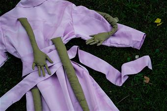 Yksityiskohta Anniina Tirin Hyvä on tässä? -malliston takista, 2022. Kuvassa takki on nurmikolla ja siitä lähtee kädenoloisia ulokkeita.