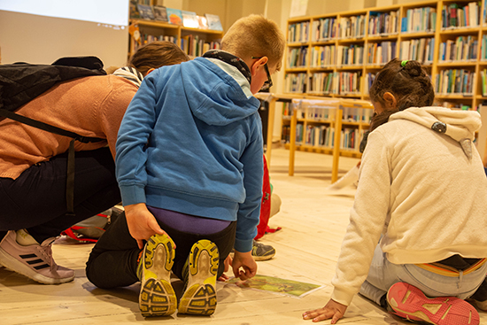 Lapset ja opettaja kumartuneena hyönteistä esittävän valokuvan äärelle.