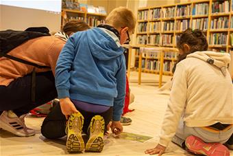 Lapset ja opettaja kumartuneena hyönteistä esittävän valokuvan äärelle.