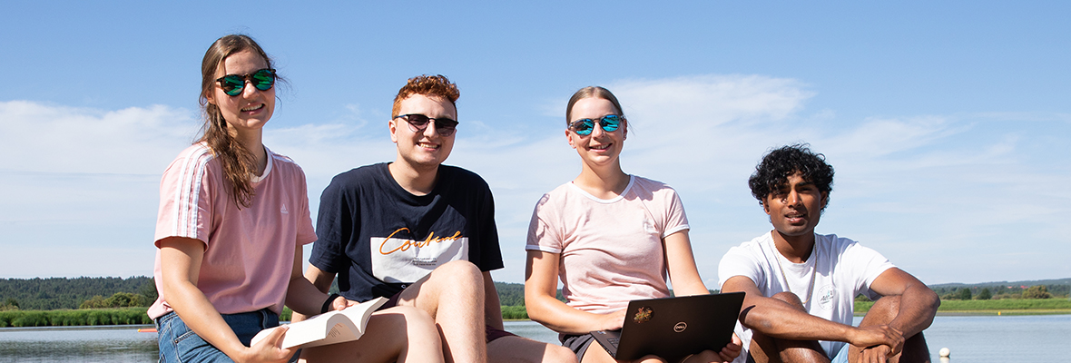 Neljä opiskelijaa istuu kesällä veden äärellä Rovaniemellä.