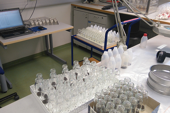 Laboratoriotarvikkeita, näytepulloja ja tietokone.