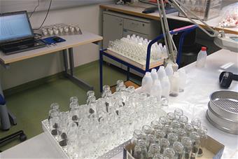 Laboratoriotarvikkeita, näytepulloja ja tietokone.