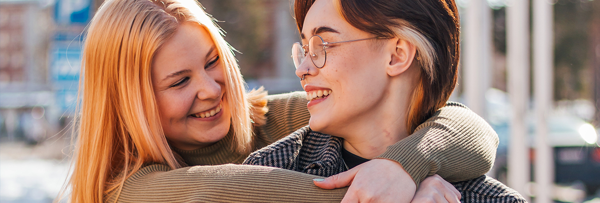 Kaksi opiskelijaa halaamassa iloisesti toisiaan yliopiston pihalla