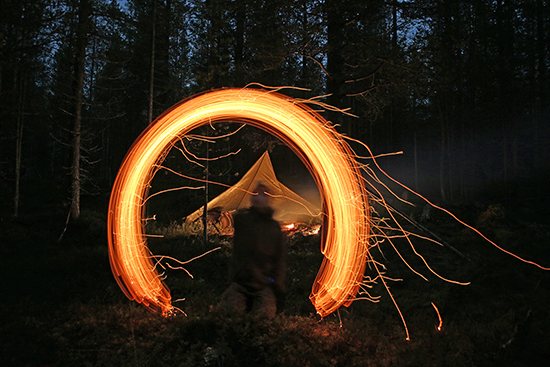 Ihminen pimeässä metsässä ilmaan maalatun tuliteoksen keskellä. Kuva: Antti Stöckell.