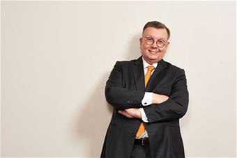 Hymyilevä Petteri Uoti nojaa seinään kädet ristissä rinnalla.