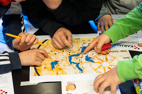 Pöydällä on aarrekartta, jota lapset osoittavat sormillaan. 