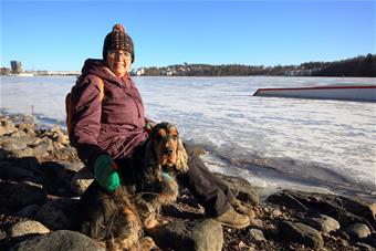 Kuvassa Riitta Penttinen istuu talvimaisemassa merenrannalla koiran kanssa. 