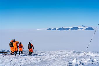 Tutkijat kävelemässä avarassa lumimaisemassa Antarktiksella.