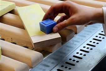 Käsi pitelee muovikuutiota puukappaleen yllä. Kuva: Siiri Paananen.