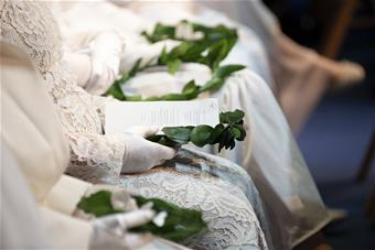 Valkoisissa mekoissa ihmisiä käsissään laakeriseppele.