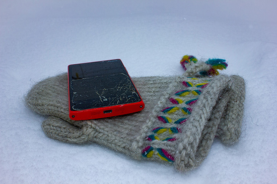 Lumen päällä villalapaset ja niiden päällä matkapuhelin, jonka lasi on rikkoutunut.