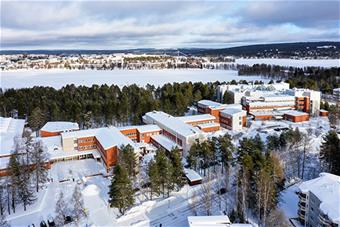 Lapin yliopiston pääkampus Rovaniemellä talvella, taustalla Rovaniemen kaupungin keskustan rakennuksia ja talvista metsää, vesistöjä ja vaaramaisemia. Kuva: Ville Rinne.